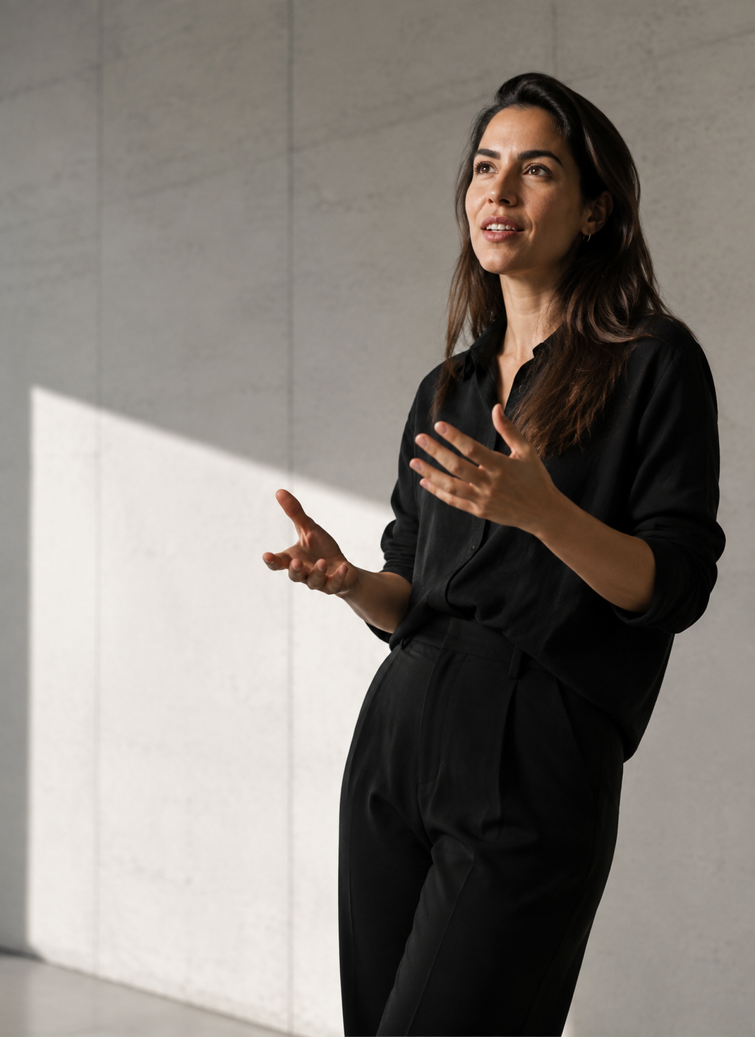 Comunicador em roupa preta, em movimento, num ambiente de concreto e parede branca com luz lateral precisa